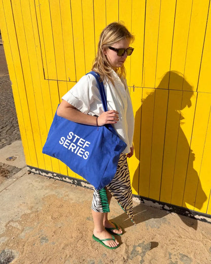 Canvas totebag in royal blue with STEF SERIES logo print worn by fashion designer Sam Van Dyck