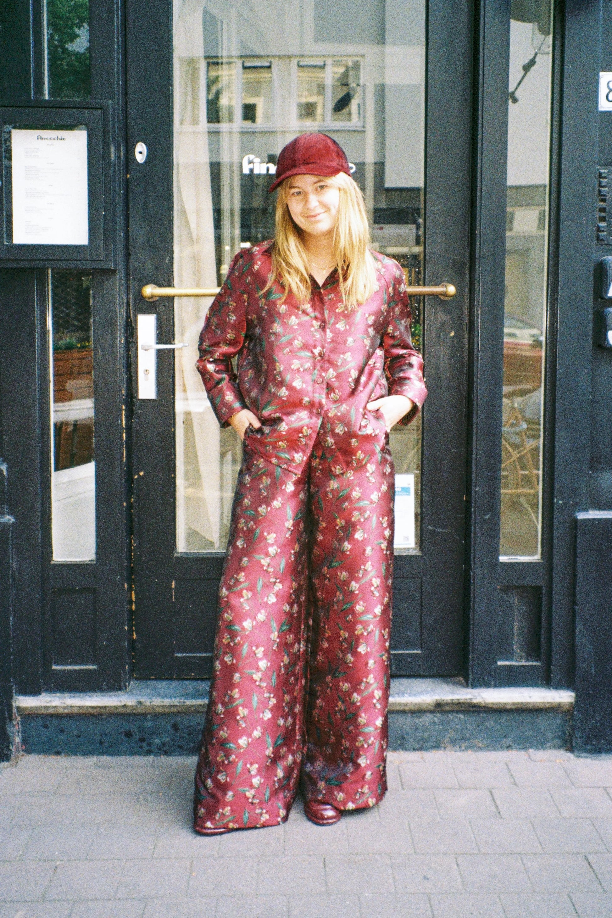 STEF SERIES founder and designer Sam Van Dyck proudly wearing her Caro wide-leg pants combined with the Coby shirt, both in a red floral print.